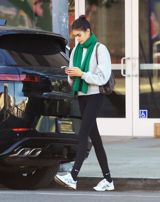 A photo of Kaia Gerber pairing a gray sweatshirt with black leggings, black Nike socks, and a bright green knit scarf.