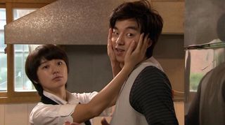 A short woman dressed as a man holds a taller man's face in her hands, in 'Coffee Prince.'