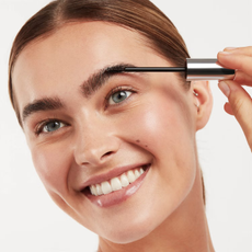 A woman using an Eyeko eyebrow gel on her eyebrows.