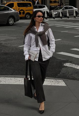 a photo of a woman's classic outfit idea with a white button-down shirt, black trousers, a gray cardigan, and black pointed pumps