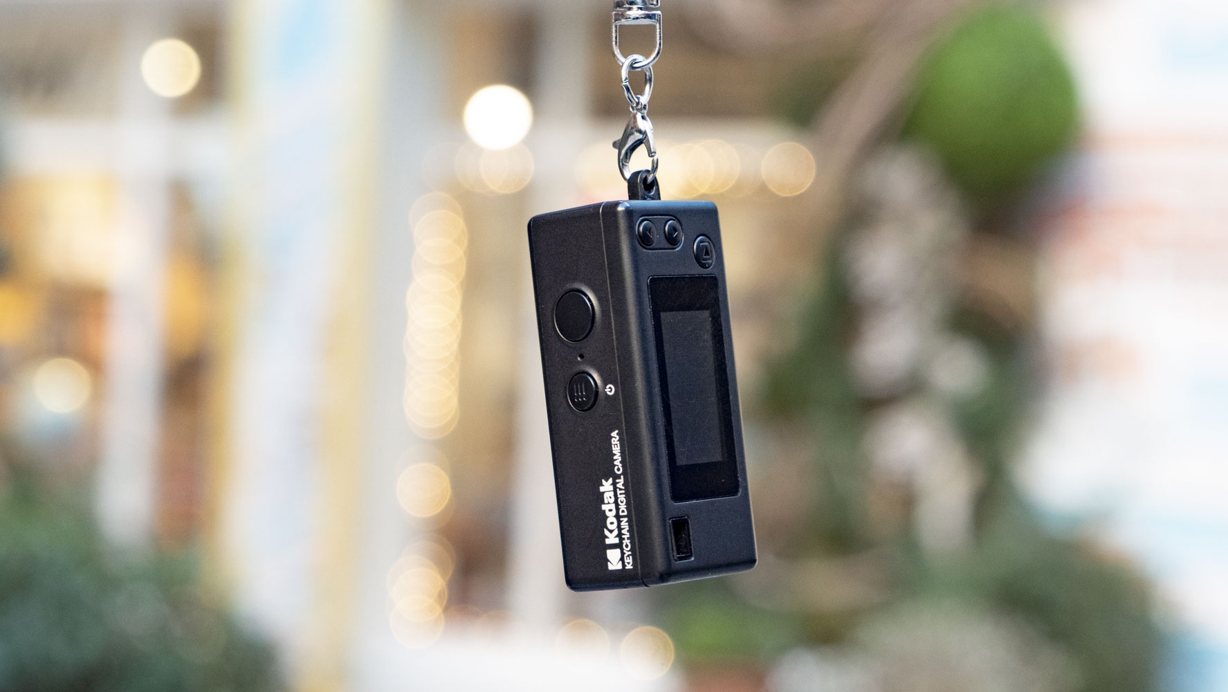 Kodak Charmera compact camera dangling from its keychain, with shop frontage backdrop