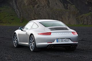 Daytime image, silver Porsche 911 Carrera S, parked on a gravel surface, hilly mountain backdrop