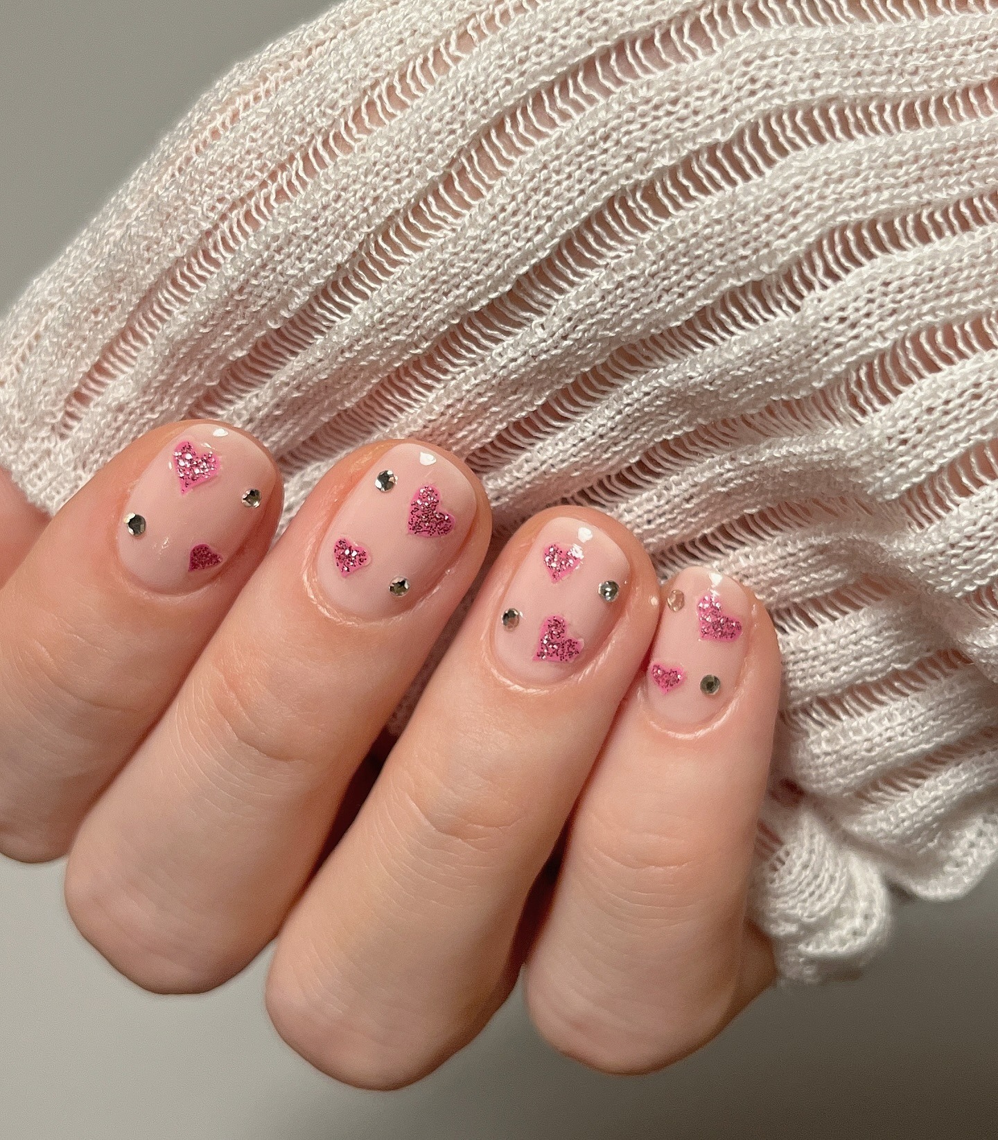 A nude manicure with pink, glittery hearts