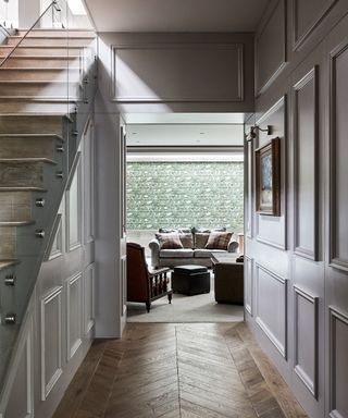 Small hallway ideas, with herringbone floor and pale gray wood panelled walls looking towards a living space.