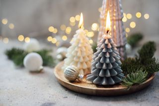 A wooden tray with two burning candles in the shape of Christmas trees.