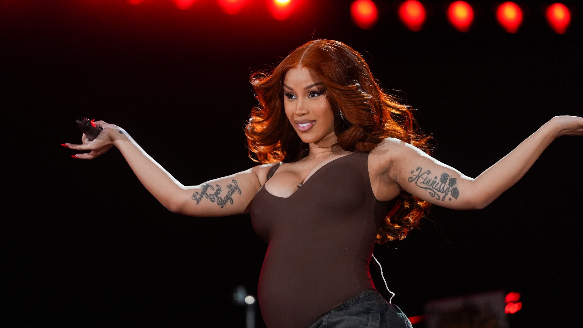 a woman performing onstage wearing long, red hair and a brown sleeveless bodysuit