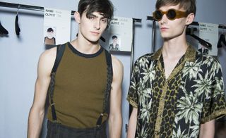 Two male models wearing clothing by Dries Van Noten in dark brown and black.