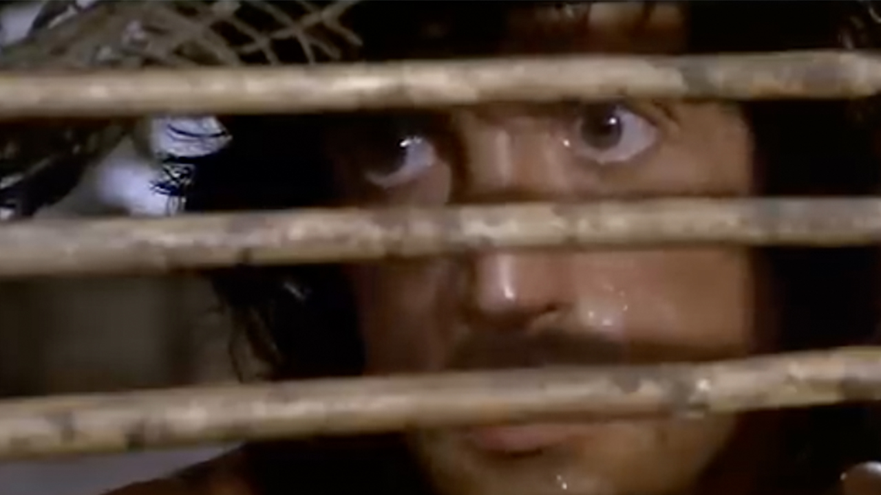 Sylvester Stallone as Rambo looking through bamboo bars in Rambo II