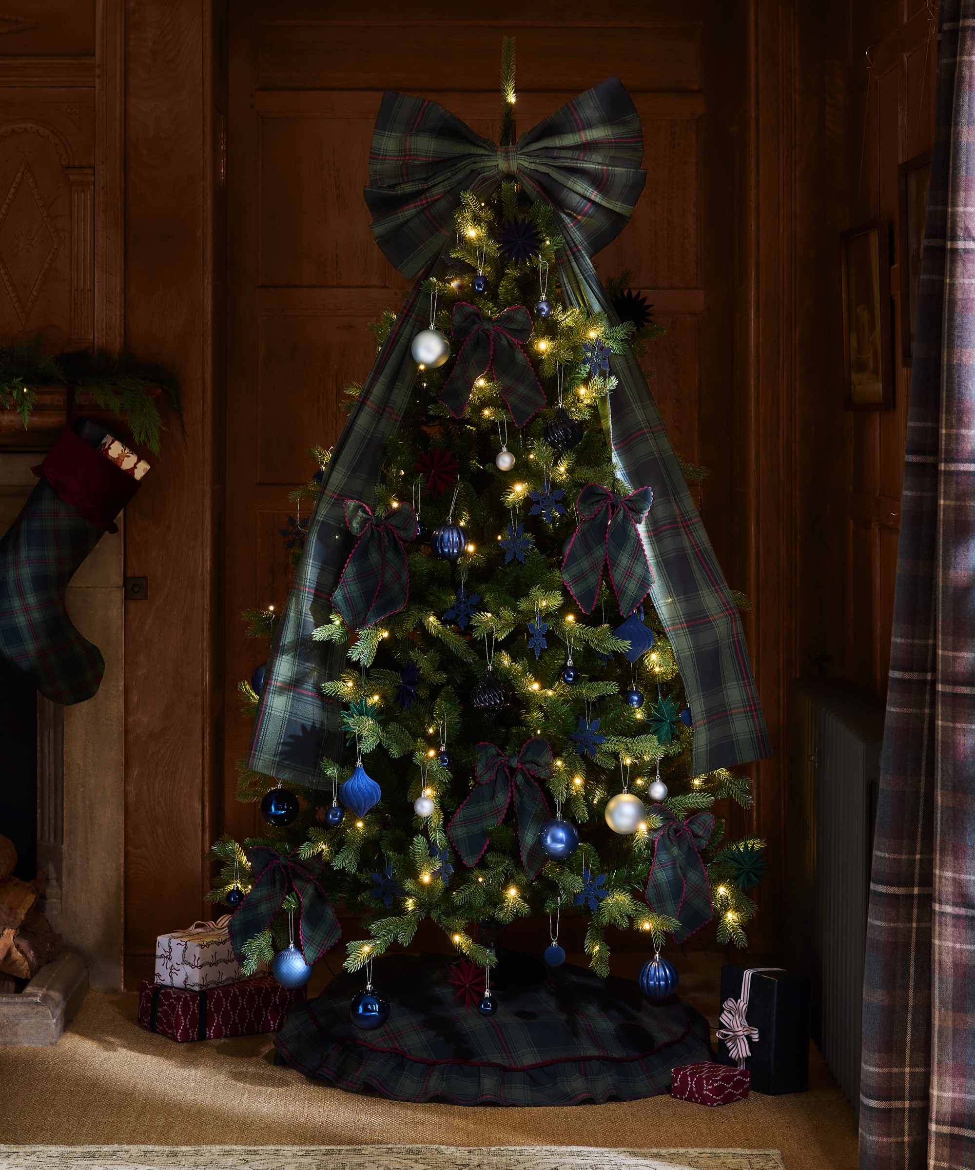 A lit-up Christmas tree decorated with Next's extra large tartan bow tree topper