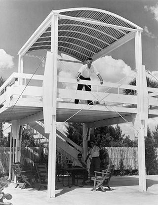 Paul Rudolph wearing a white shirt and black trousers standing on the first floor of a beach house.