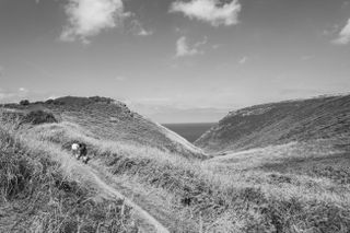 Landscape in Cornwall with hikers in the distance and the sea between two rock faces