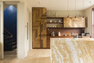 modern kitchen with timber floors, timber cabinetry, floating shelves, walnut timber backsplash, and soft yellow marble kitchen island