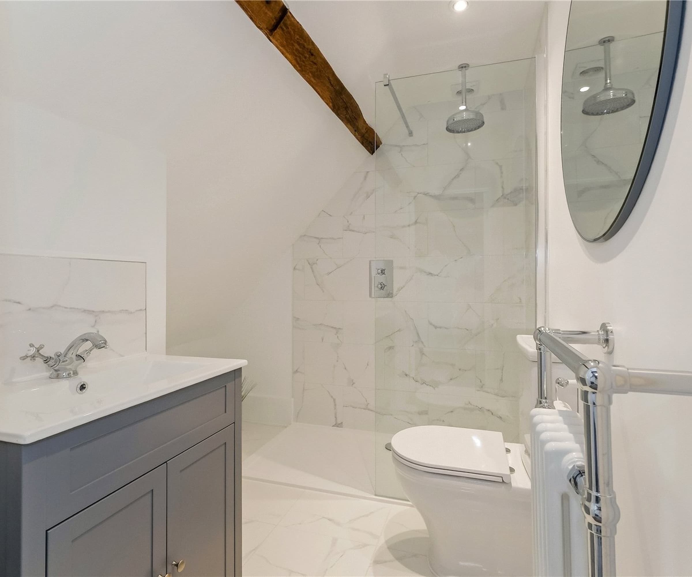 A small bathroom with a walk in shower and an oak beam above a large mirror on wall