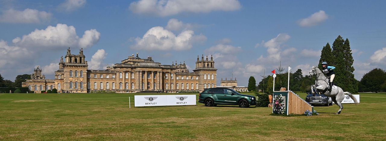 A grey horse jumps a skinny cross-country fence in front of Blenheim Palace, the venue of Blenheim International Horse Trials