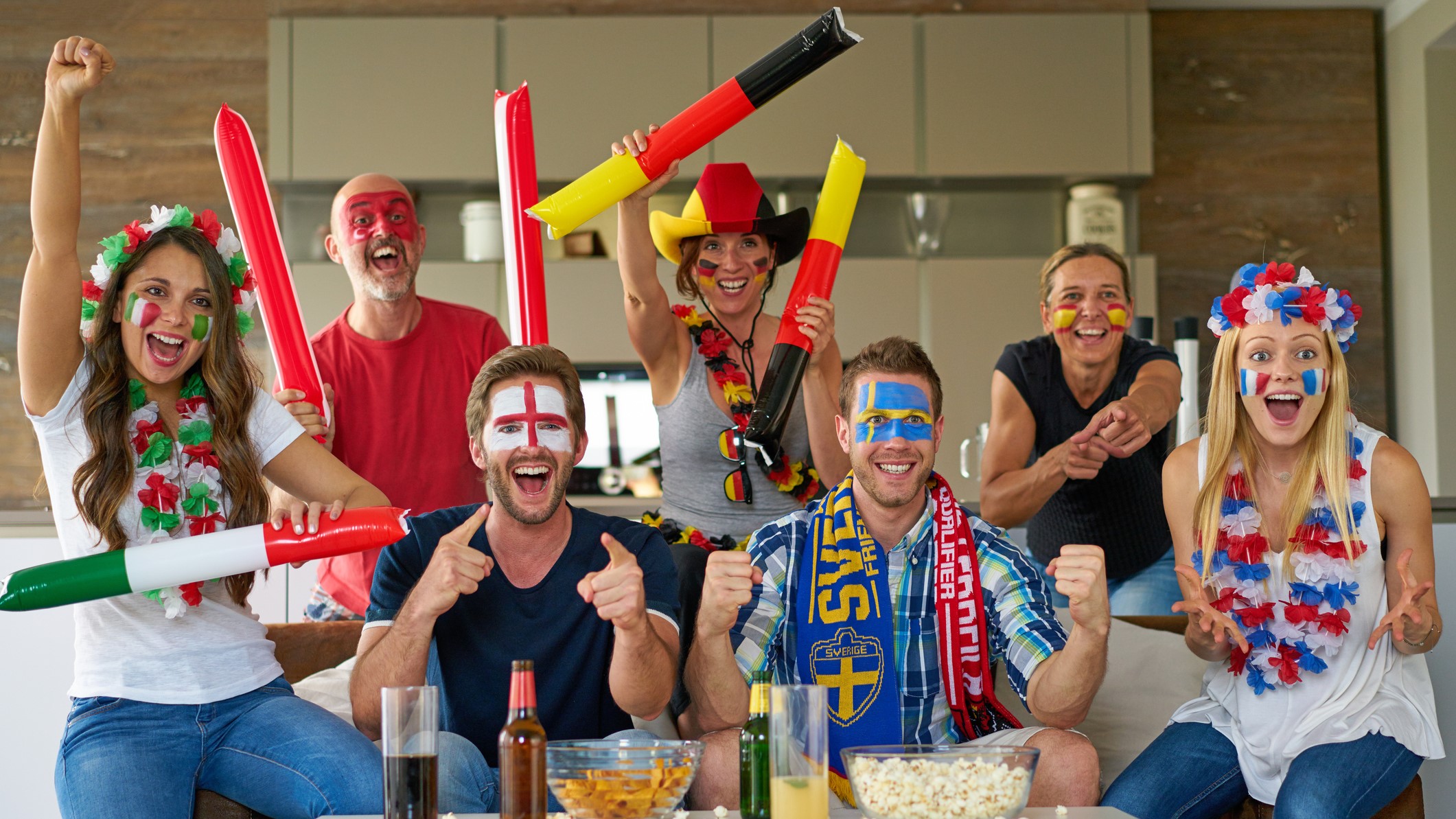 People from different countries cheering while watching the football match on the sofa