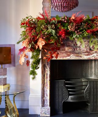 A white fireplace mantel with a large, lush real pine garland with red flowers