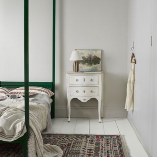 small bedroom colour ideas, very pale grey bedroom with white floorboards, white vintage side table, artwork, green painted four poster bed, vintage rug