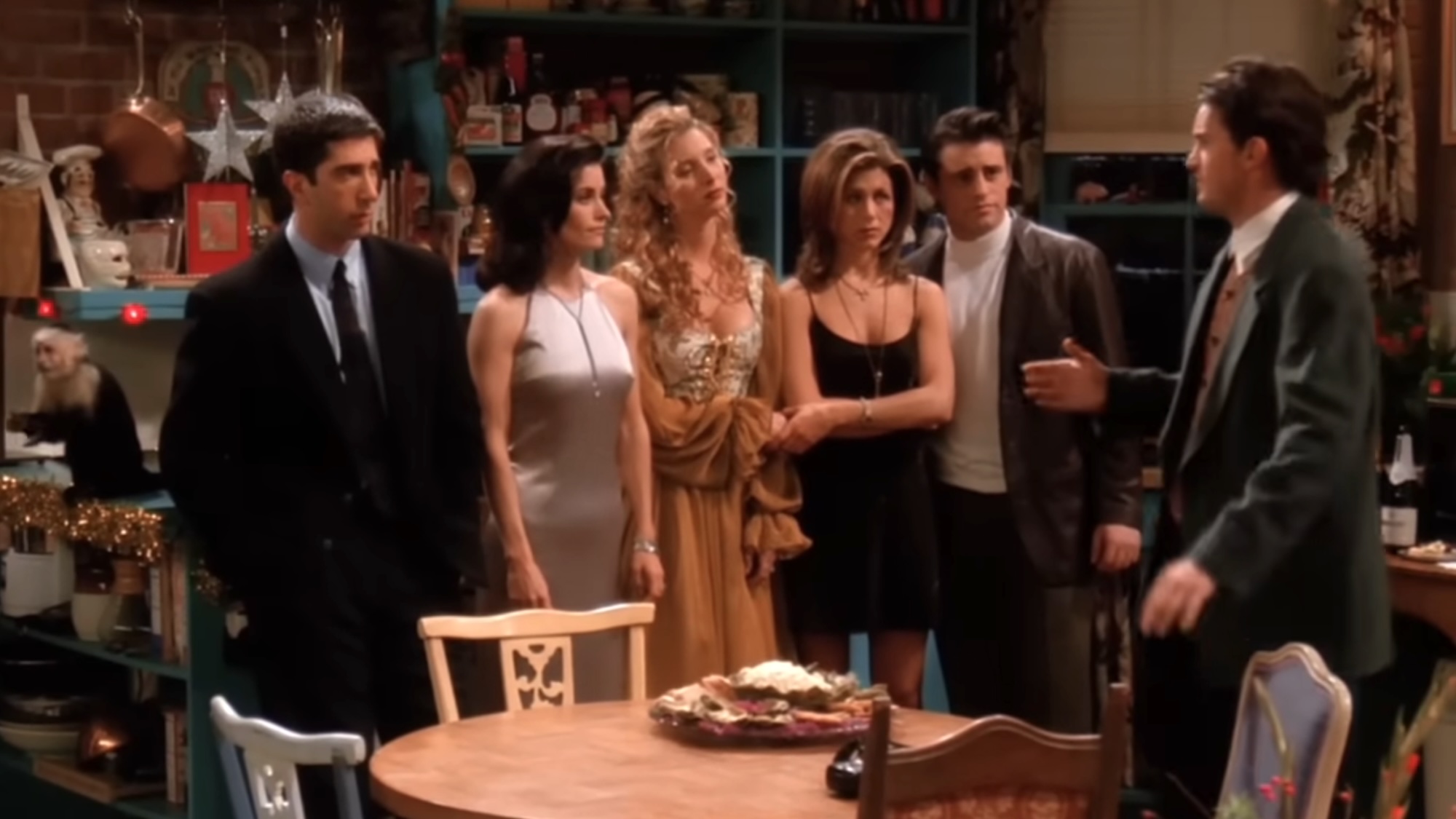 The cast of Friends standing around the kitchen table. 