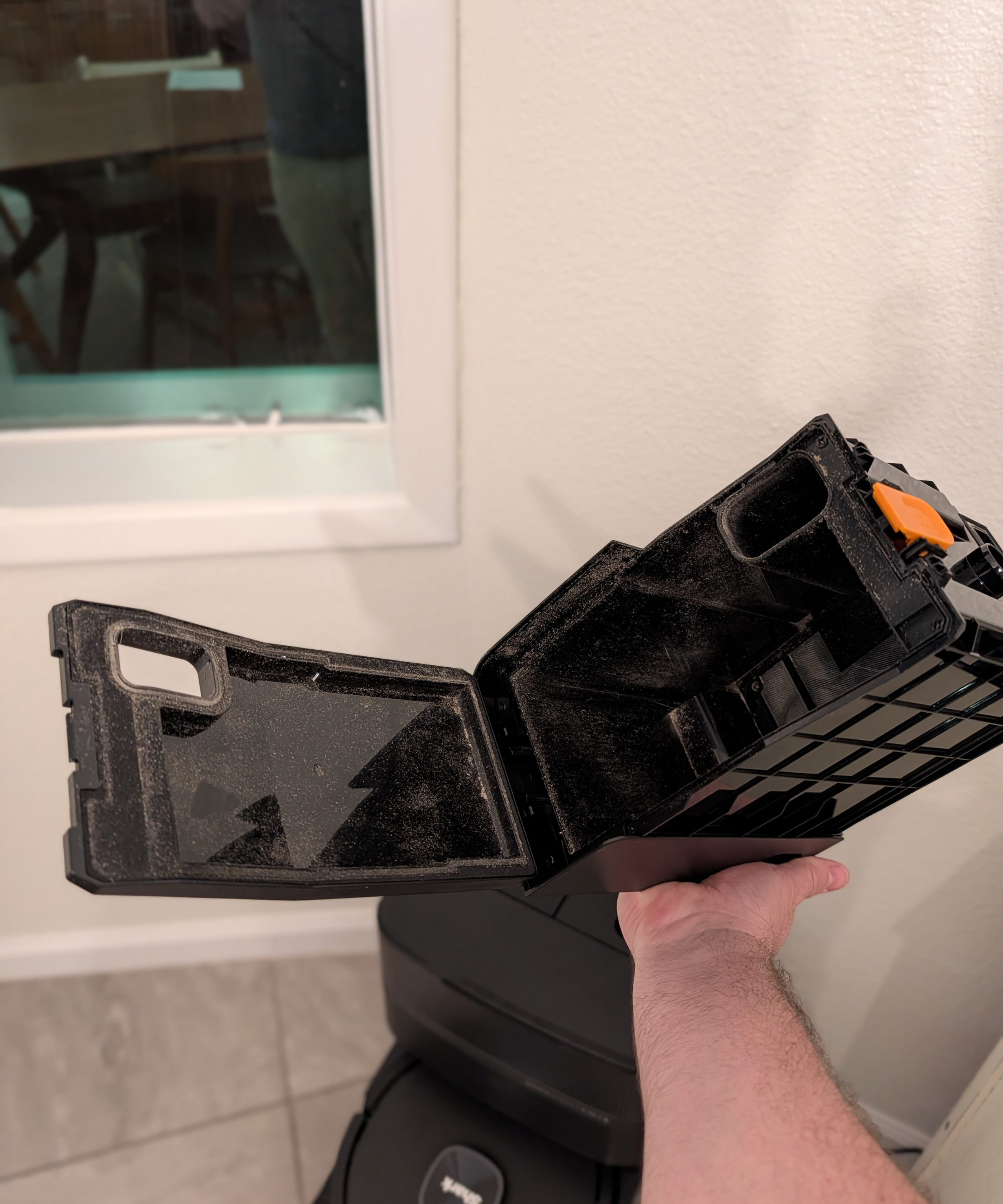A man holding the dock dust bin of the Shark PowerDetect UV Reveal in front of a white wall with a window.