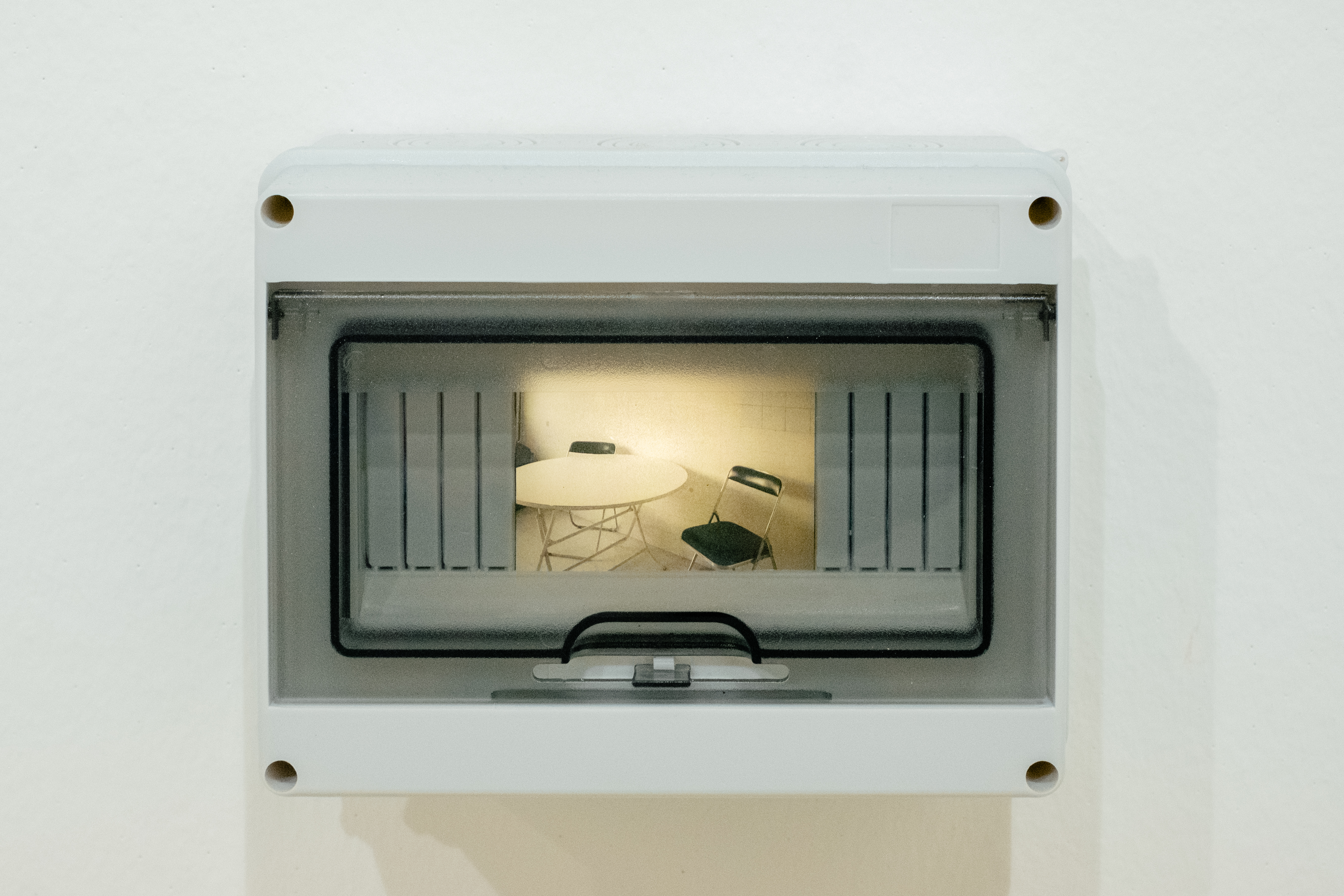 A chandelier glowing with warm light is captured in a photograph back-lit inside an electricity box as part of an art installation.
