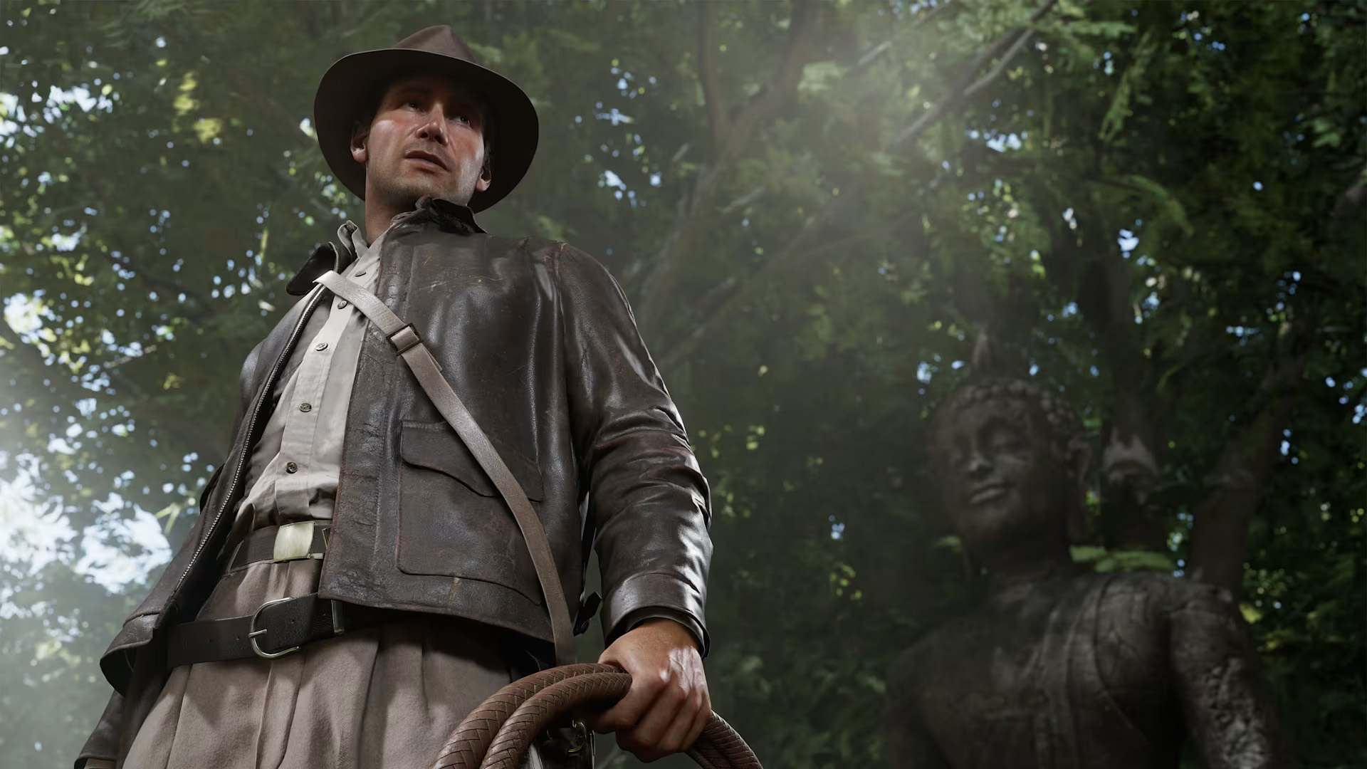 Screenshot from Indiana Jones and the Great Circle showing Indy from a top down position holding his whip in front of a statue and some trees 