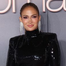 jennifer lopez attends a film premiere wearing a black gown and poses in front of a gray background