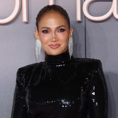 jennifer lopez attends a film premiere wearing a black gown and poses in front of a gray background