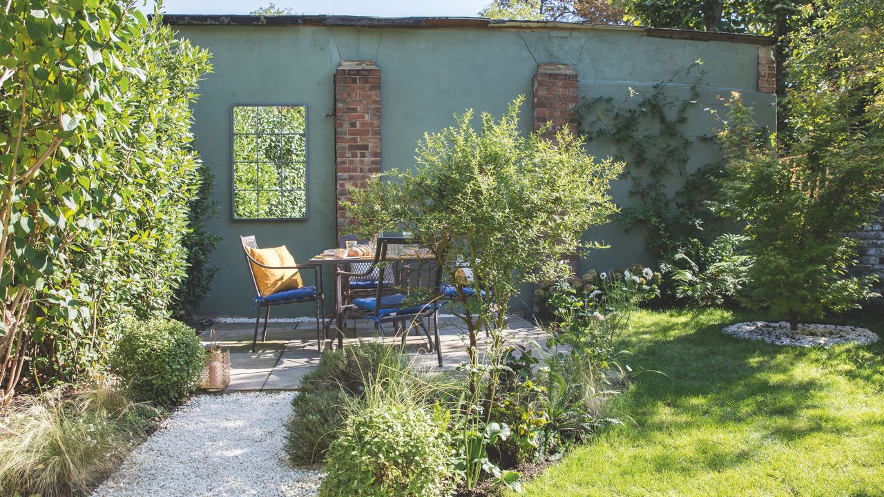 Gravel path through the garden leading to a seating area with table and chairs beside a green wall. Garden redesign of a small city garden in London, owned by Rosie Money-Coutts.