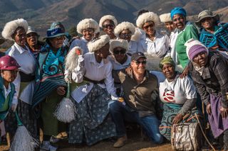 Prince Harry posing with a group of women in Lesotho in front of a mountain