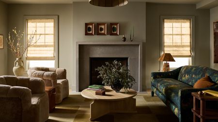 a cozy living room in a Federal-style home with original fireplace, two small windows, a tapestry print couch, shearling armchairs and rounded tables