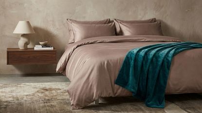 A bedroom with a raw plaster wall, pink silk bedding, and a floating nightstand