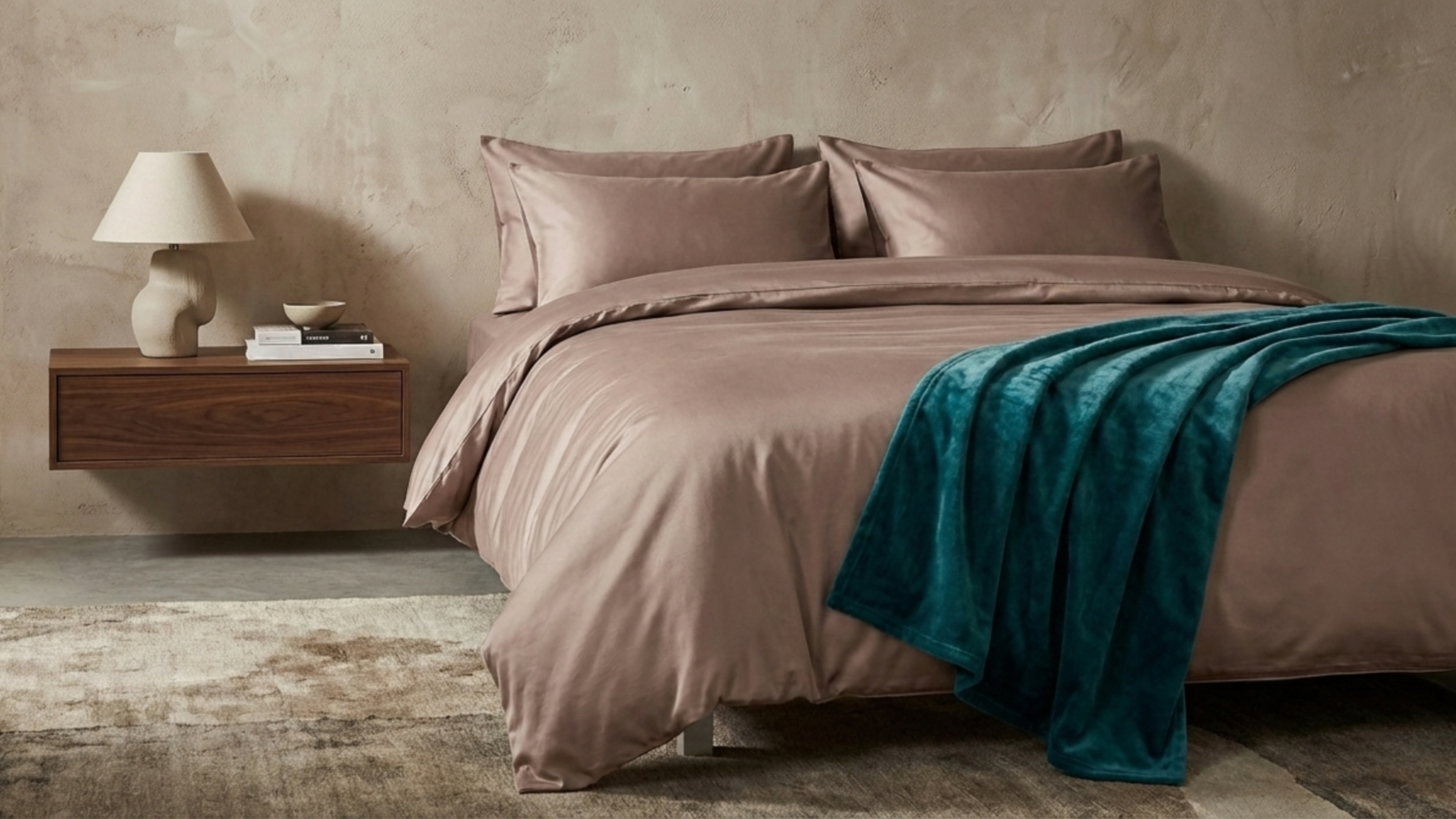 A bedroom with a raw plaster wall, pink silk bedding, and a floating nightstand