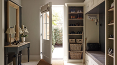 A bright entryway with an open glass-frame door, black side table with mirror above to the left, with lamps and flowers on it, and shelves and a bench to the right.