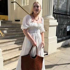 Woman wears white dress and carries tan woven leather bag