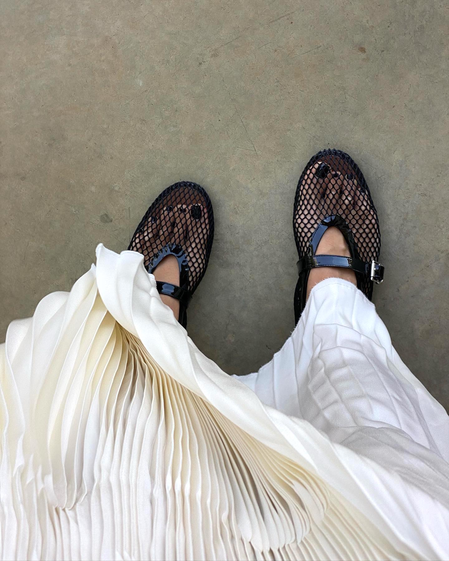 fashion influencer Débora Rosa takes a photo of her pleated white satin skirt and Alaïa mesh Mary Jane flats