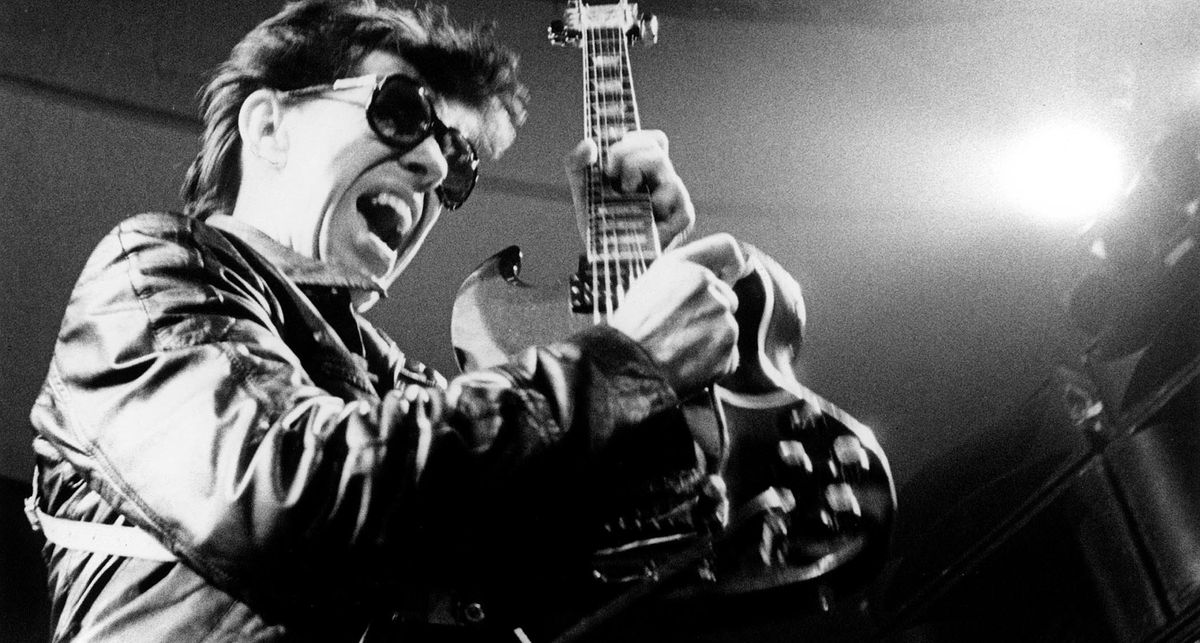 A black and white action shot of Link Wray behind dark sunglasses, bending a note on a Gibson SG and making it squeal