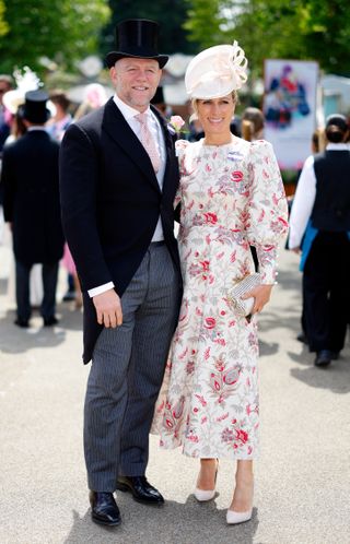 Mike Tindall wearing a suit and top hat and Zara Tindall wearing a white and red printed dress and hat standing outside