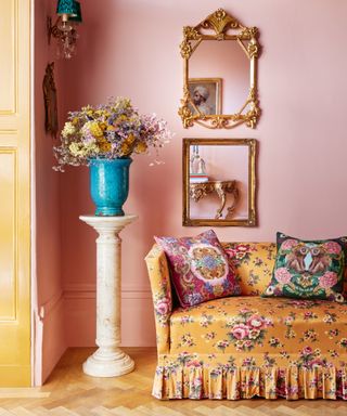 Plaster pink living room with yellow couch, ornate mirrors, vase, decorative pillows
