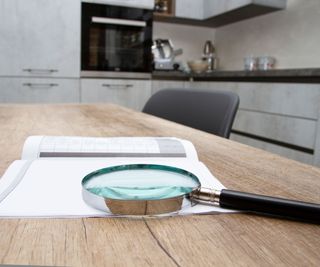 An open instruction manual on a kitchen table with a magnifying glass on top