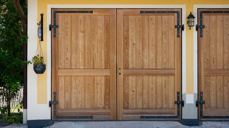 Finding out how to get rid of mice from a garage is useful. Here is a garage with wooden doors, framed with yellow and white walls with black wall sconces and a hanging basket 