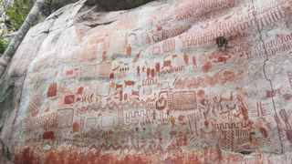 A massive rock wall covered in red-colored rock art