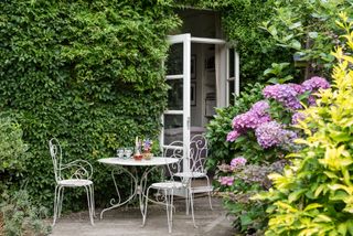 A small garden with a small white wrought iron table and chairs