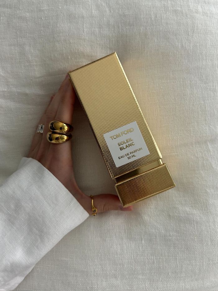 Młodsza redaktorka ds. urody Grace Lindsay trzyma perfumy Toma Forda Soleil Blanc w złotym pudełku