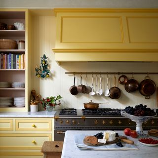 Kitchen with yellow units, cream walls, parquet flooring and large range cooker with saucepans hanging on the wall above