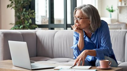 A woman with gray hair looks at a laptop and thinks.