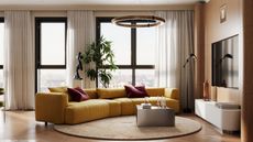 Image of a luxury, modern living room with large windows lining the walls. There is a large ochre yellow sofa in the center of the room with red throw pillows. In front of the sofa is a silver chrome coffee table.