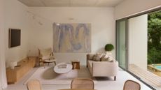 A minimalist living room with a framed TV, a wood sideboard, rattan chairs, a woolly sofa chair, a linen sofa, and a coffee table, by a large painting