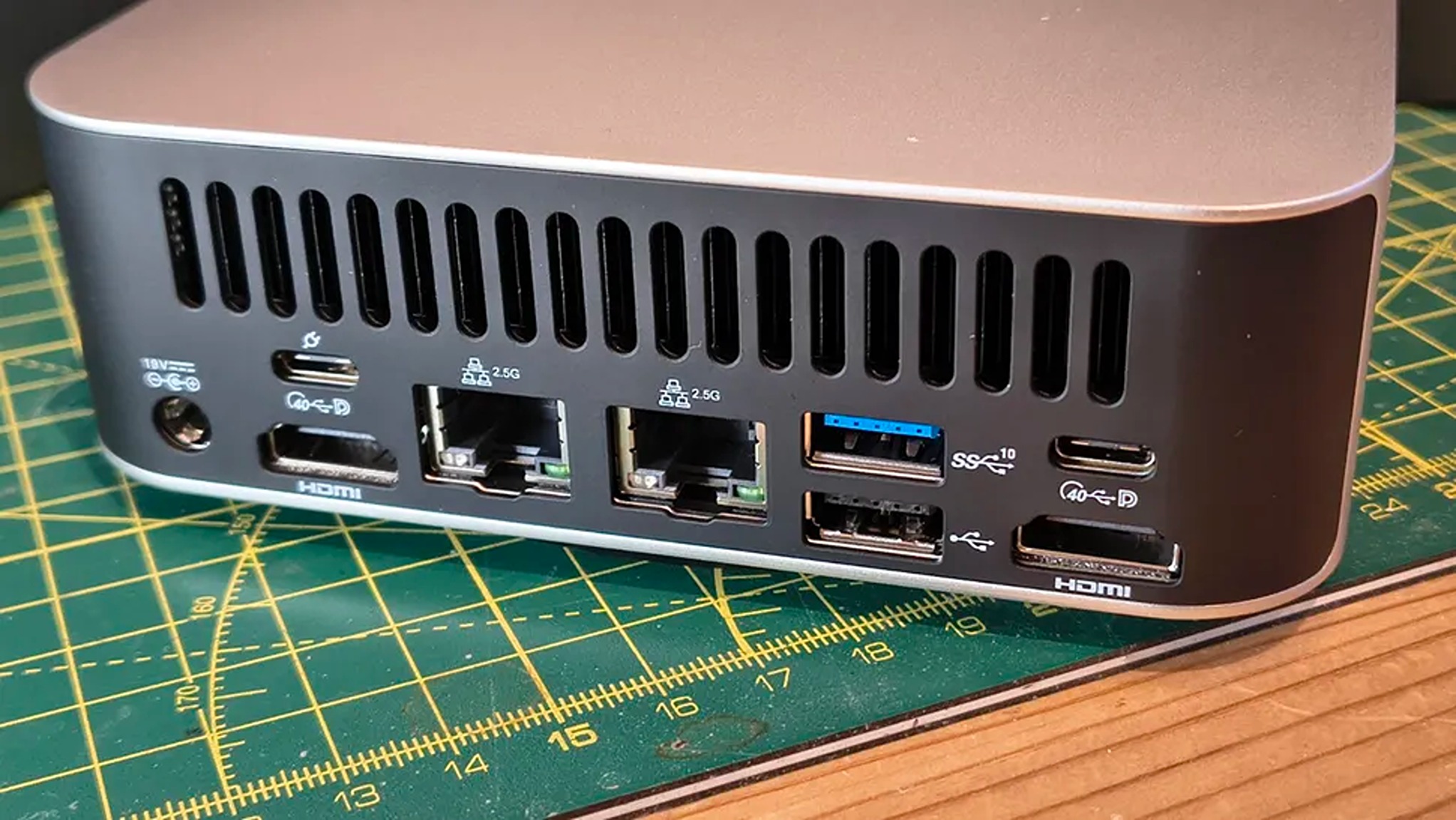Rear view of a compact gray computer on a cutting mat, showing multiple ports: USB, HDMI, Ethernet, and USB-C, suggesting versatile connectivity.