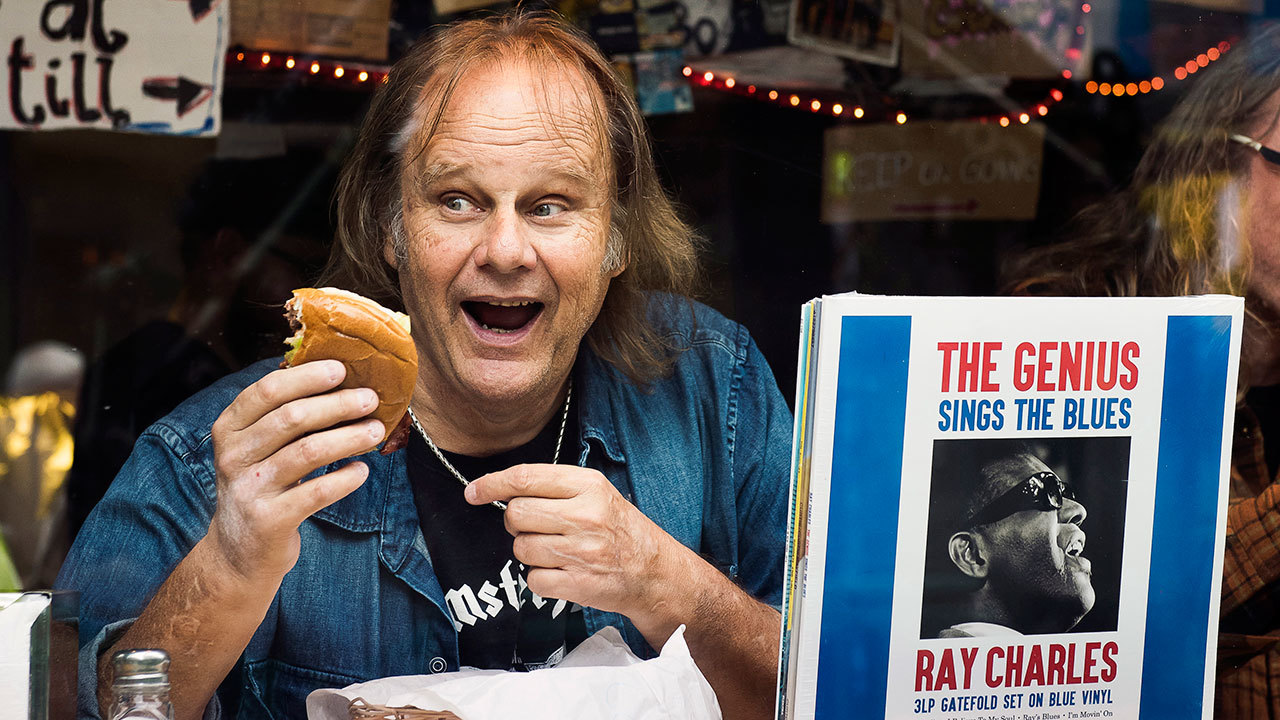 A portrait of walter trout eating a burger with some records