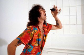 Bon Scott in a Hawaiian shirt, drinking a glass of wine